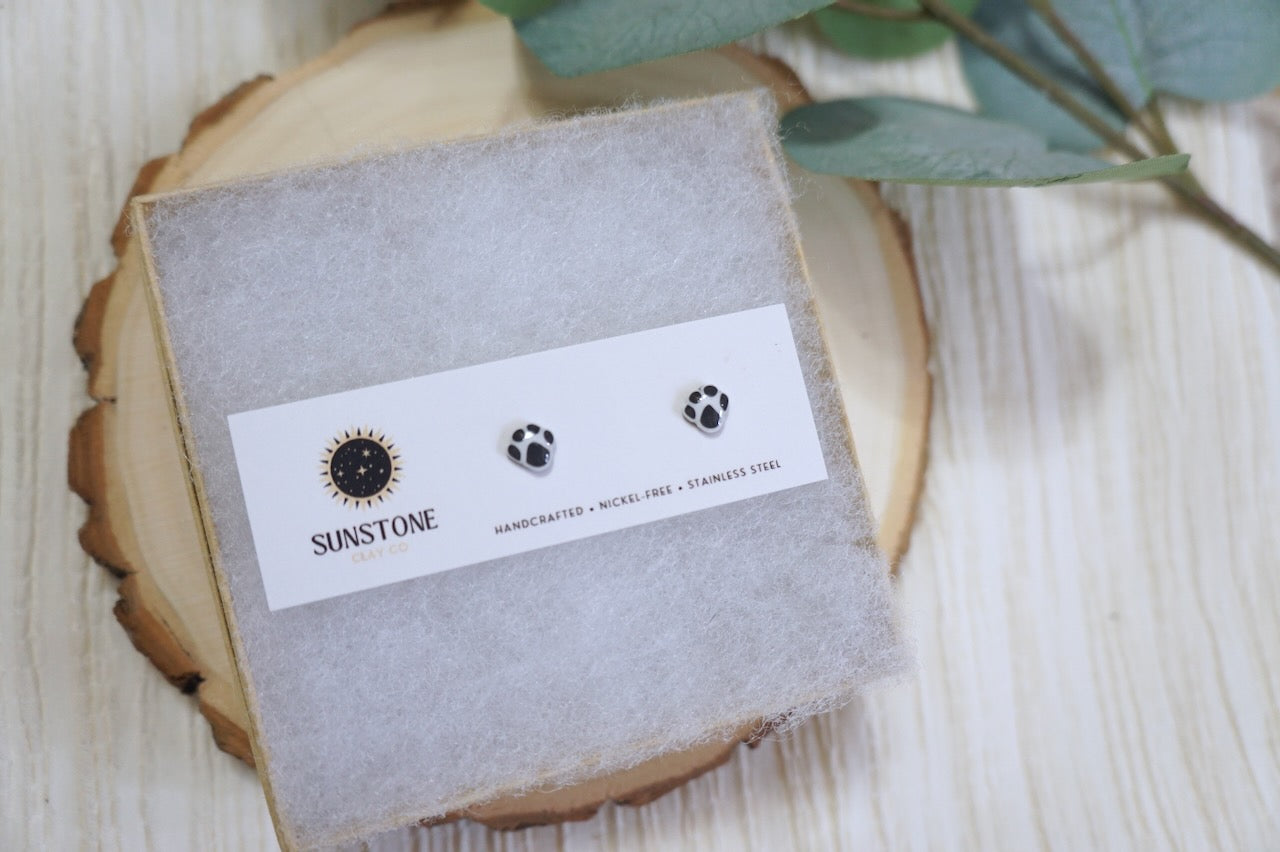 Black and white paw print stud earrings on Sunstone Clay Co. display card