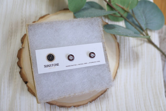 Handcrafted UGA football stud earrings with red, black, and white “G” logo displayed on a Sunstone Clay Co. earring card on a wooden background.
