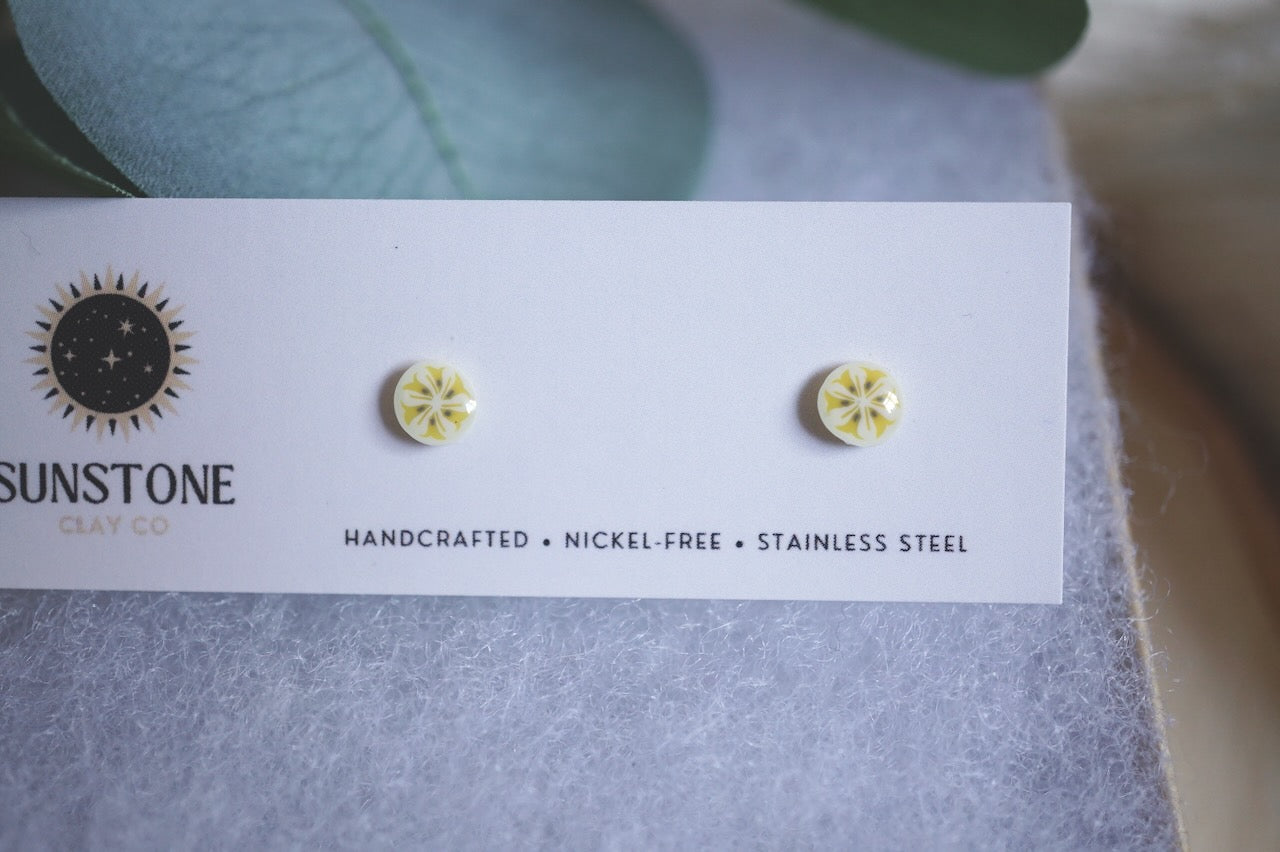 Handmade tiny banana slice stud earrings displayed on Sunstone Clay Co card.