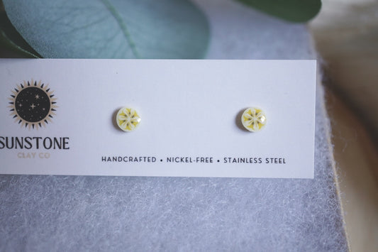 Handmade tiny banana slice stud earrings displayed on Sunstone Clay Co card.