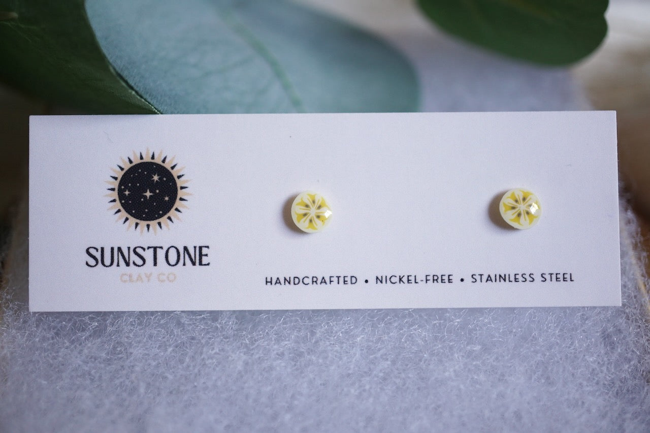Handmade tiny banana slice stud earrings displayed on Sunstone Clay Co card.