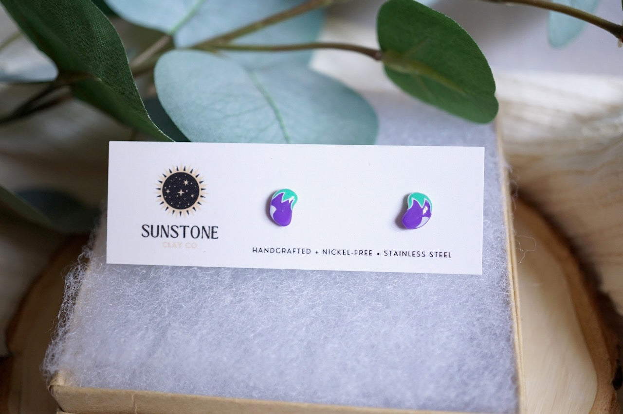 Purple polymer clay eggplant earrings with green tops on white background