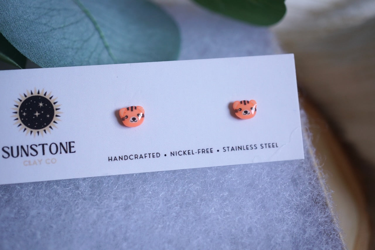 Handcrafted polymer clay tiger face stud earrings displayed on a jewelry card