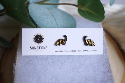 Pair of black and gold brontosaurus earrings on a Sunstone branded card with green leaves in the background.