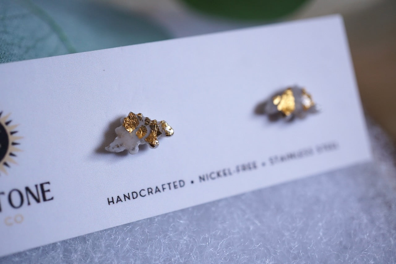 Gray and gold stegosaurus stud earrings on Sunstone Clay Co. display card.