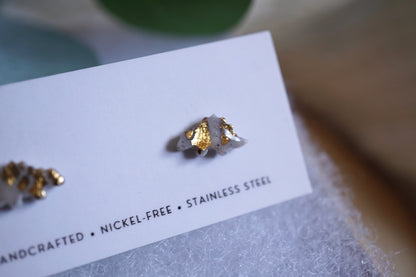 Gray and gold stegosaurus stud earrings on Sunstone Clay Co. display card.