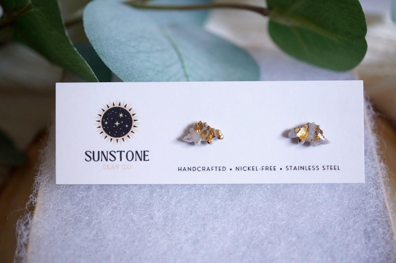 Gray and gold stegosaurus stud earrings on Sunstone Clay Co. display card.