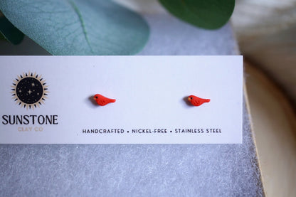 Handcrafted micro red bird stud earrings displayed on Sunstone Clay Co. card.