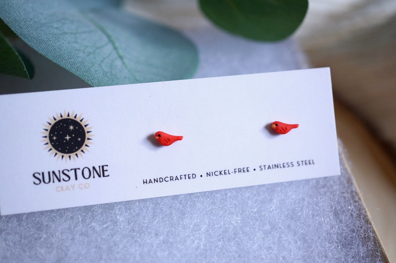 Handcrafted micro red bird stud earrings displayed on Sunstone Clay Co. card.