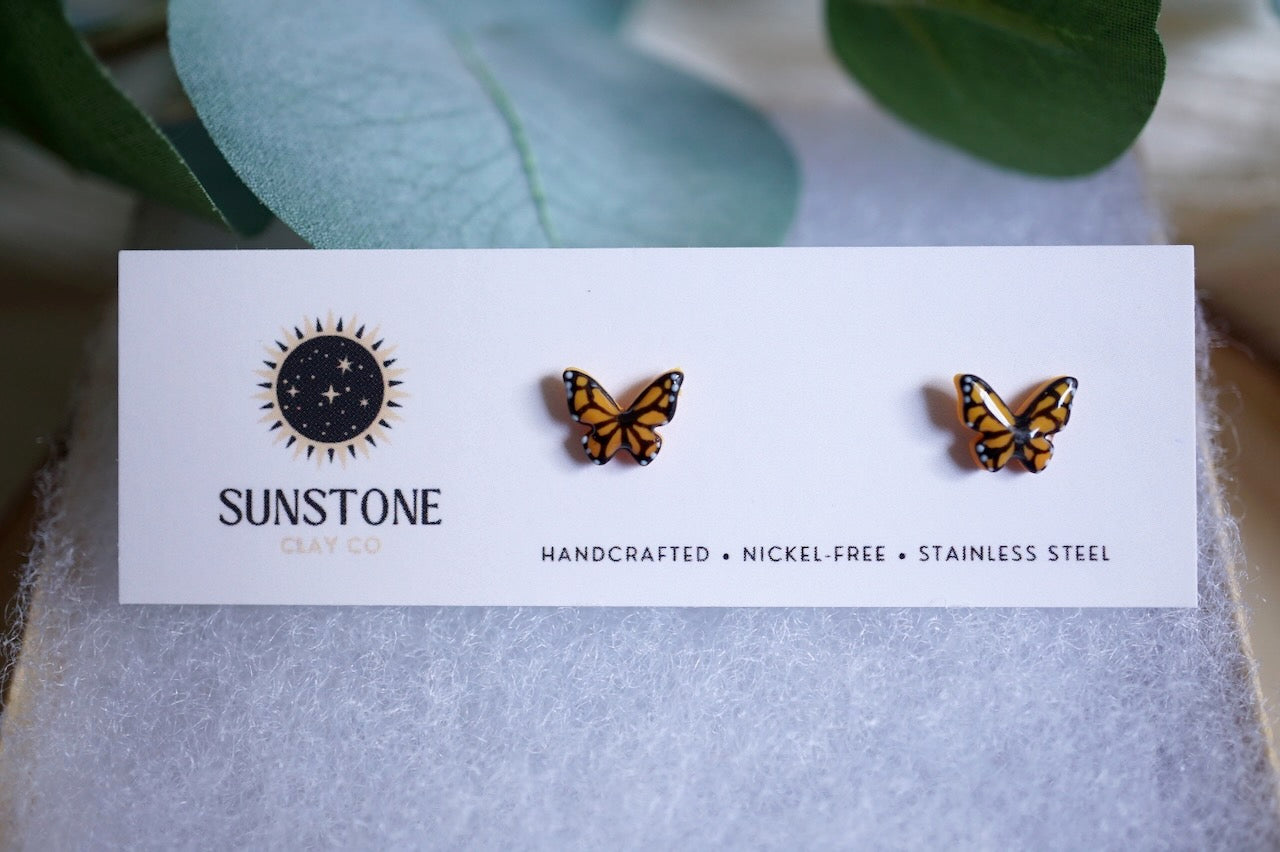 Butterfly-shaped earrings on a Sunstone Outfitters card with green leaves in the background