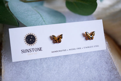 Butterfly-shaped earrings on a 'Sunstone' branded card with green leaves in the background