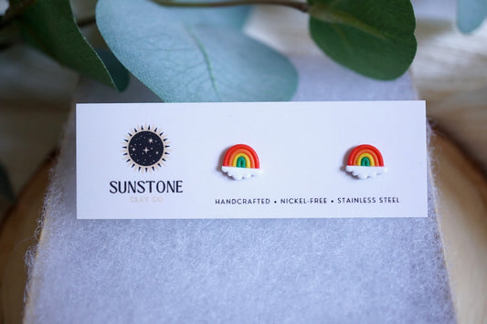Rainbow-shaped earrings on a Sunstone branded card with green leaves in the background