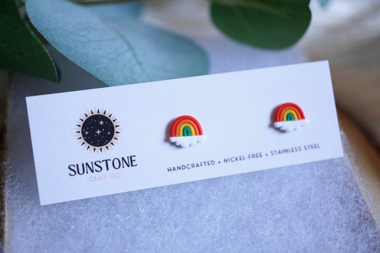 Rainbow earrings on a Sunstone branded card with green leaves in the background