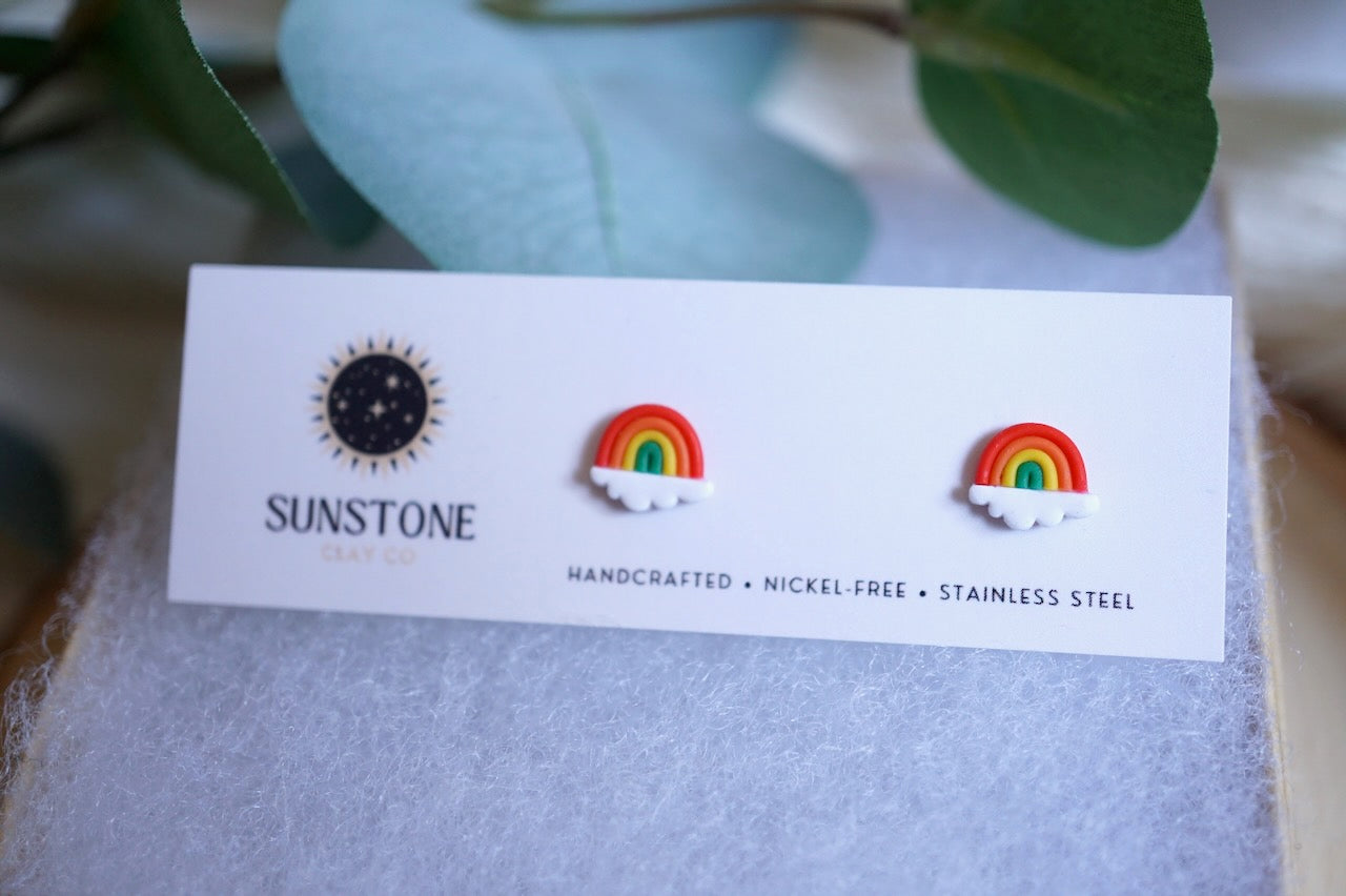 Pair of rainbow earrings on a Sunstone card with leaves in the background