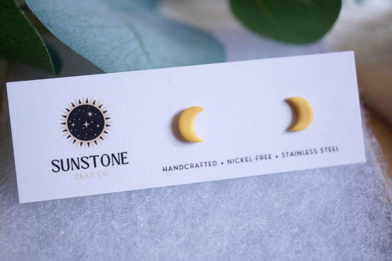 Yellow crescent moon stud earrings on Sunstone Clay Co display card