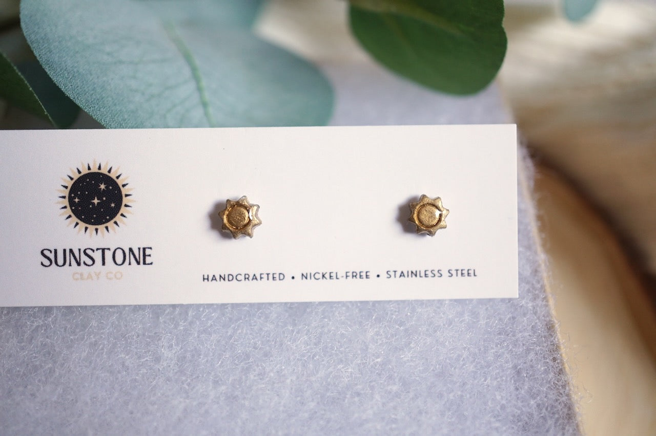 Gold earrings on a Sunstone branded card with green leaves in the background