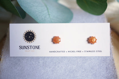 Tiny sun earrings with golden amber shimmer displayed on wood background