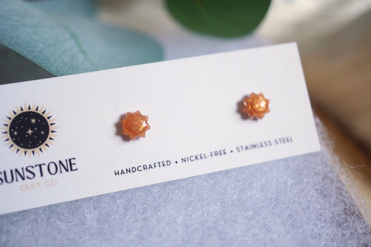 Tiny sun earrings with golden amber shimmer displayed on wood background