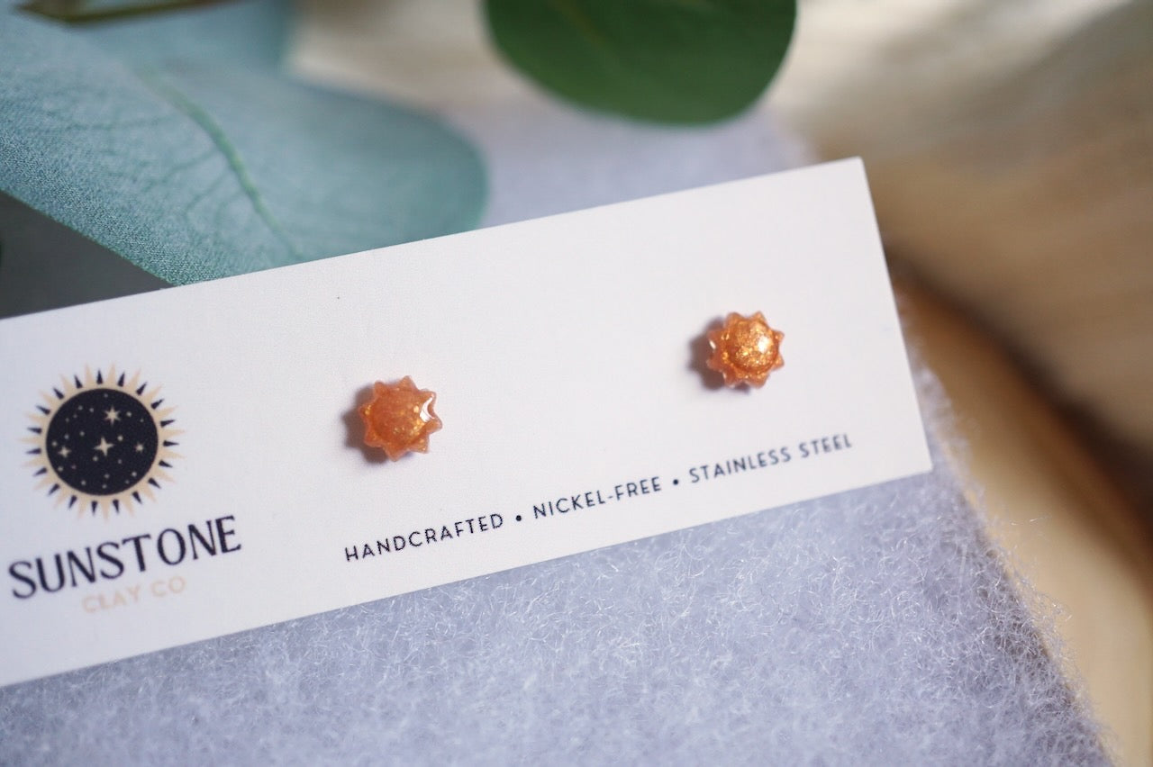 Tiny sun earrings with golden amber shimmer displayed on wood background