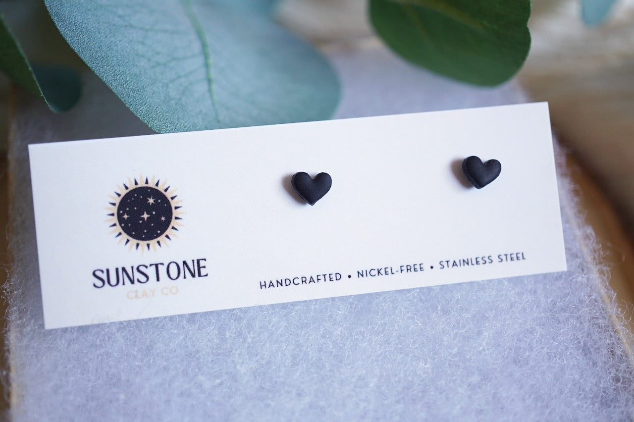 Black heart-shaped earrings on a Sunstone branded card with green leaves in the background