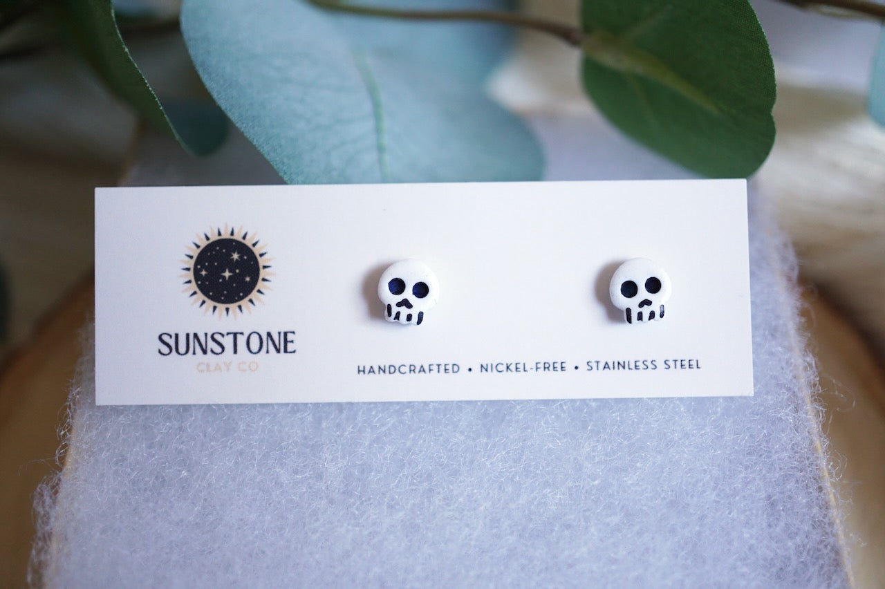 Pair of skull-shaped earrings on a Sunstone branded card with a blurred natural background
