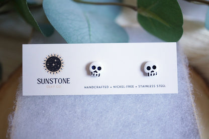 Pair of skull-shaped earrings on a Sunstone branded card with a blurred natural background