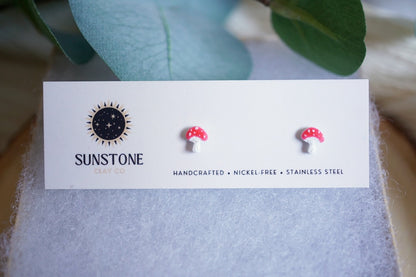 Tiny mushroom earrings on a branded card with leaves in the background