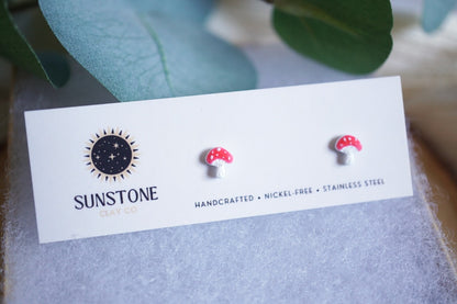 Tiny mushroom stud earrings on a branded card with green leaves in the background