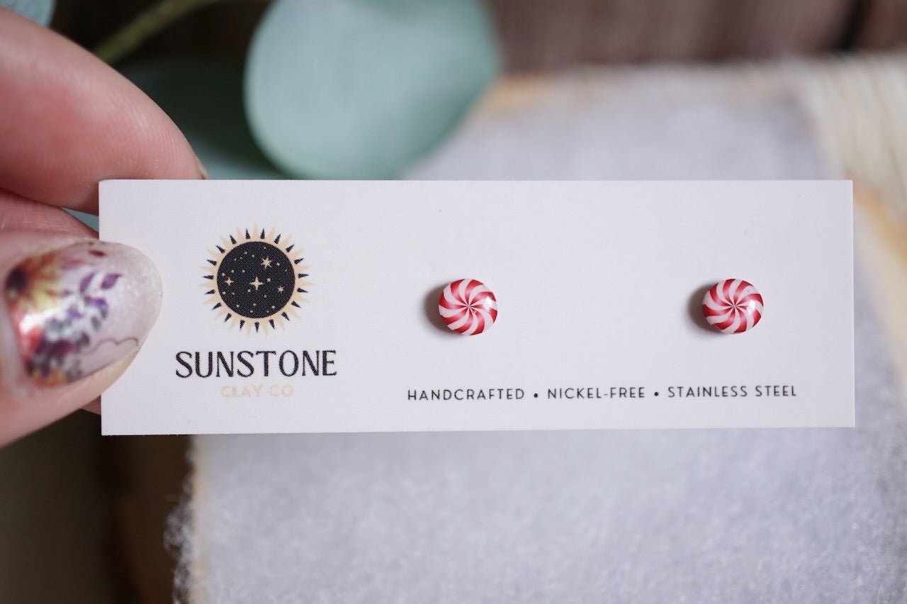 Handcrafted peppermint swirl stud earrings with red and white candy design on Sunstone Clay Co display card.