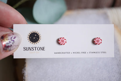 Handcrafted peppermint swirl stud earrings with red and white candy design on Sunstone Clay Co display card.
