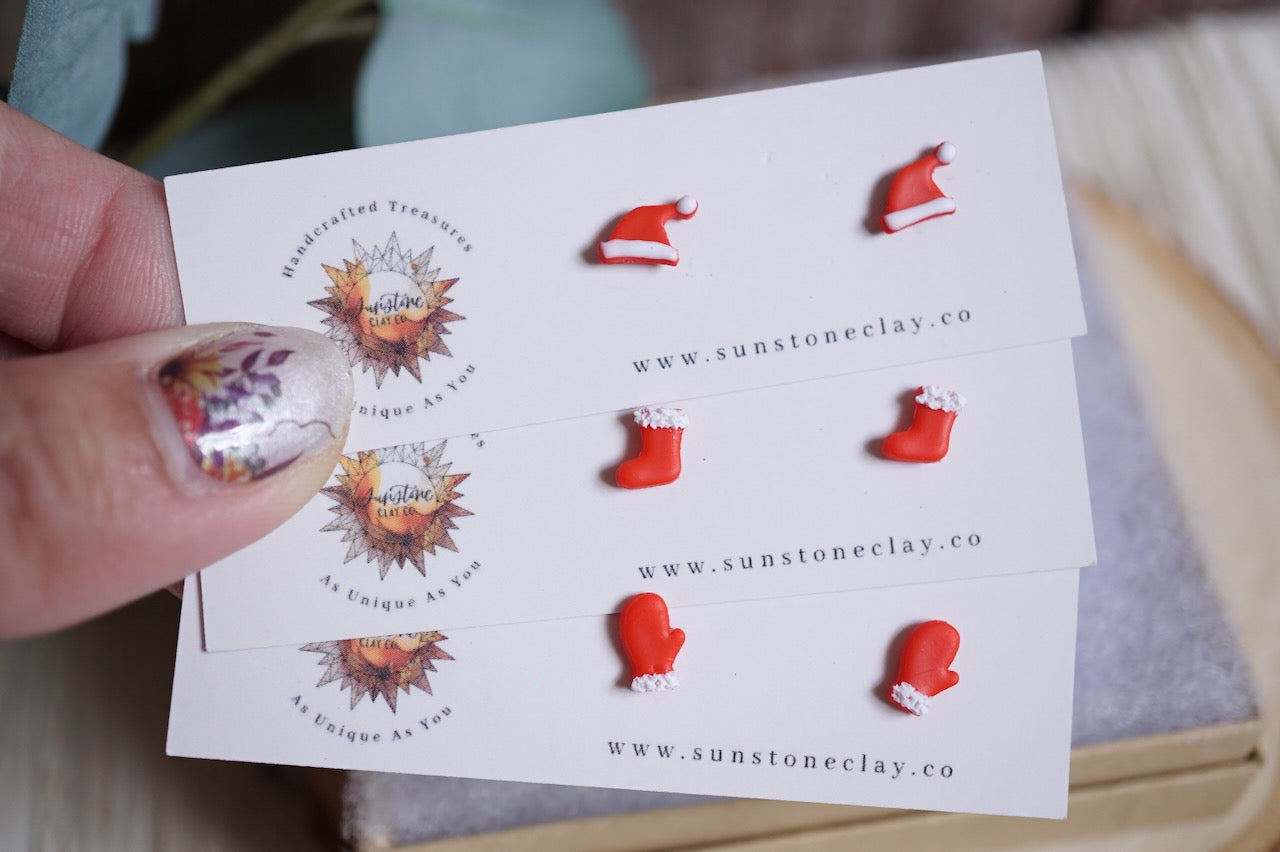 Mini handcrafted Santa hat stud earrings, stocking stud earrings, and mitten stud earrings, all in red.