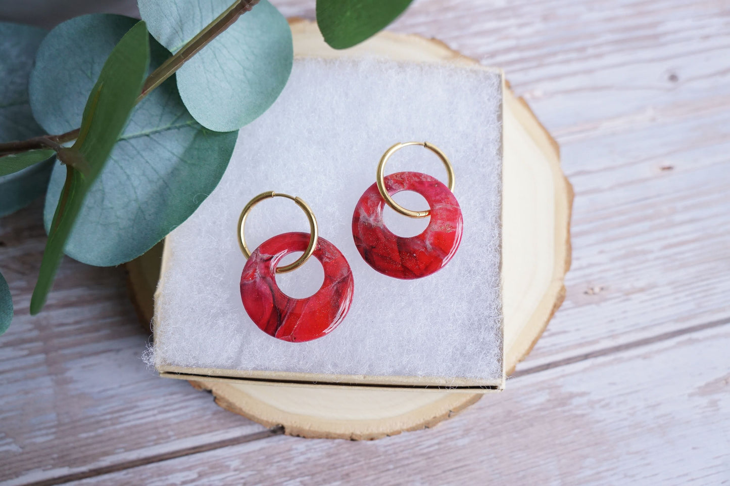 Red polymer clay earrings with gold hoops on neutral display