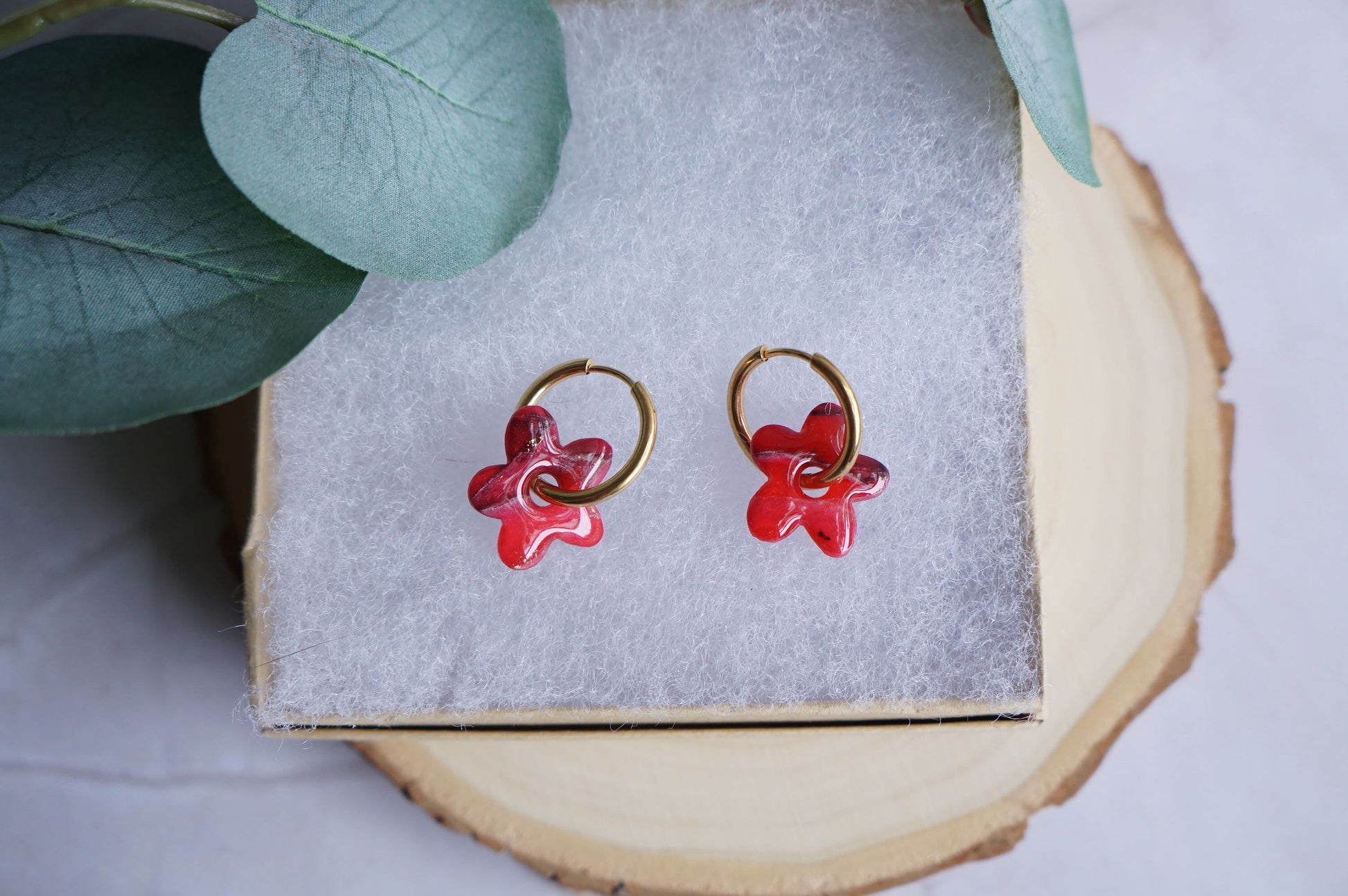 Red flower polymer clay earrings with gold hoops on neutral display