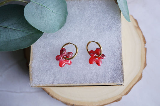 Red flower polymer clay earrings with gold hoops on neutral display