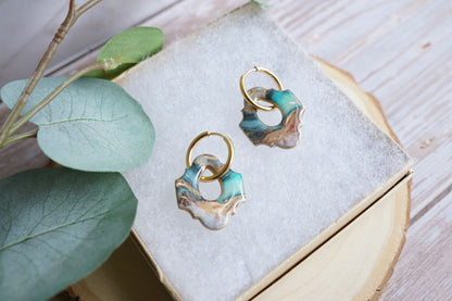 Artisan teal and gold earrings styled on soft fabric display