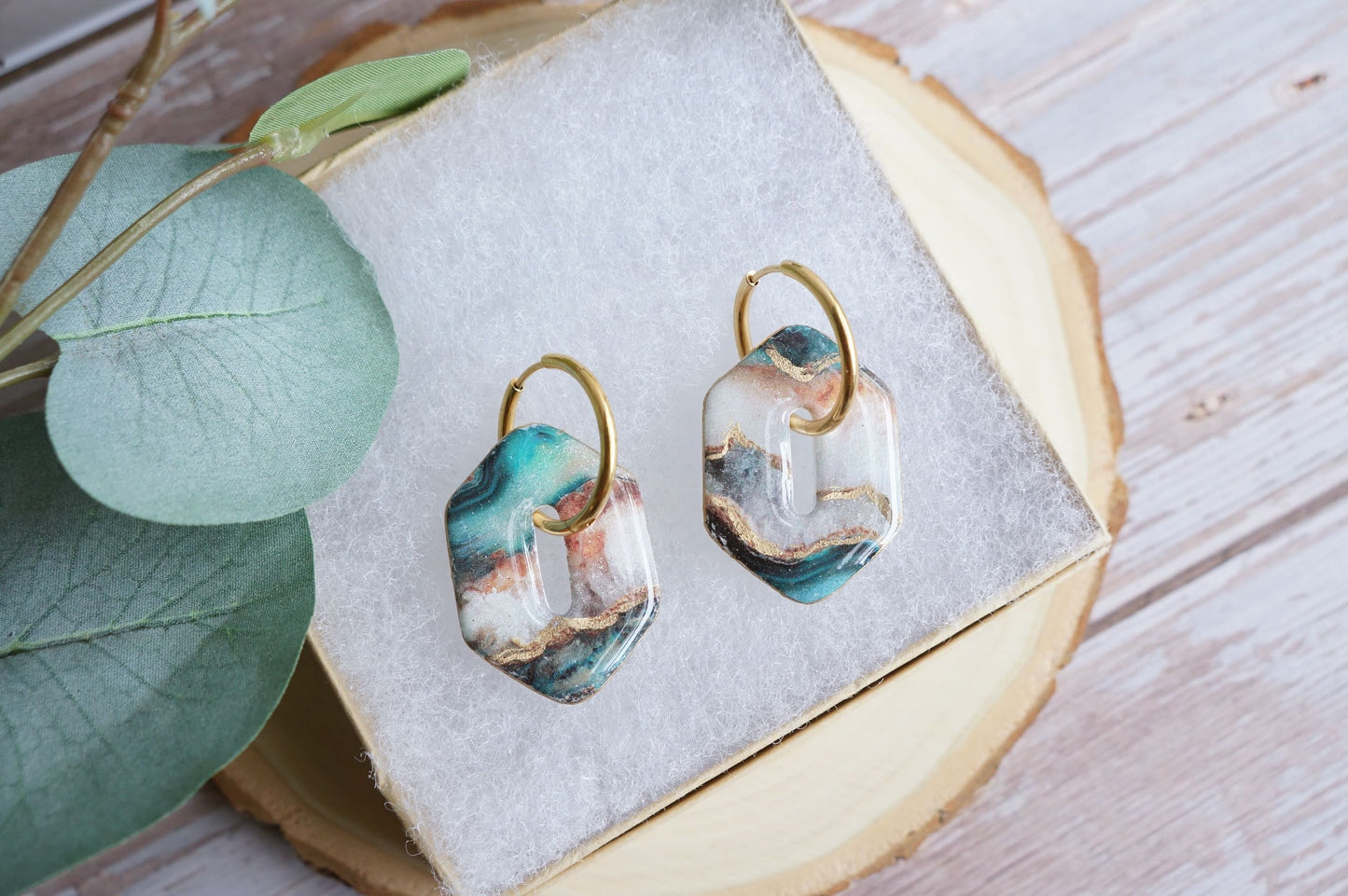 Artisan teal and gold earrings styled on soft fabric display