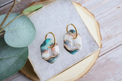 Artisan teal and gold earrings styled on soft fabric display