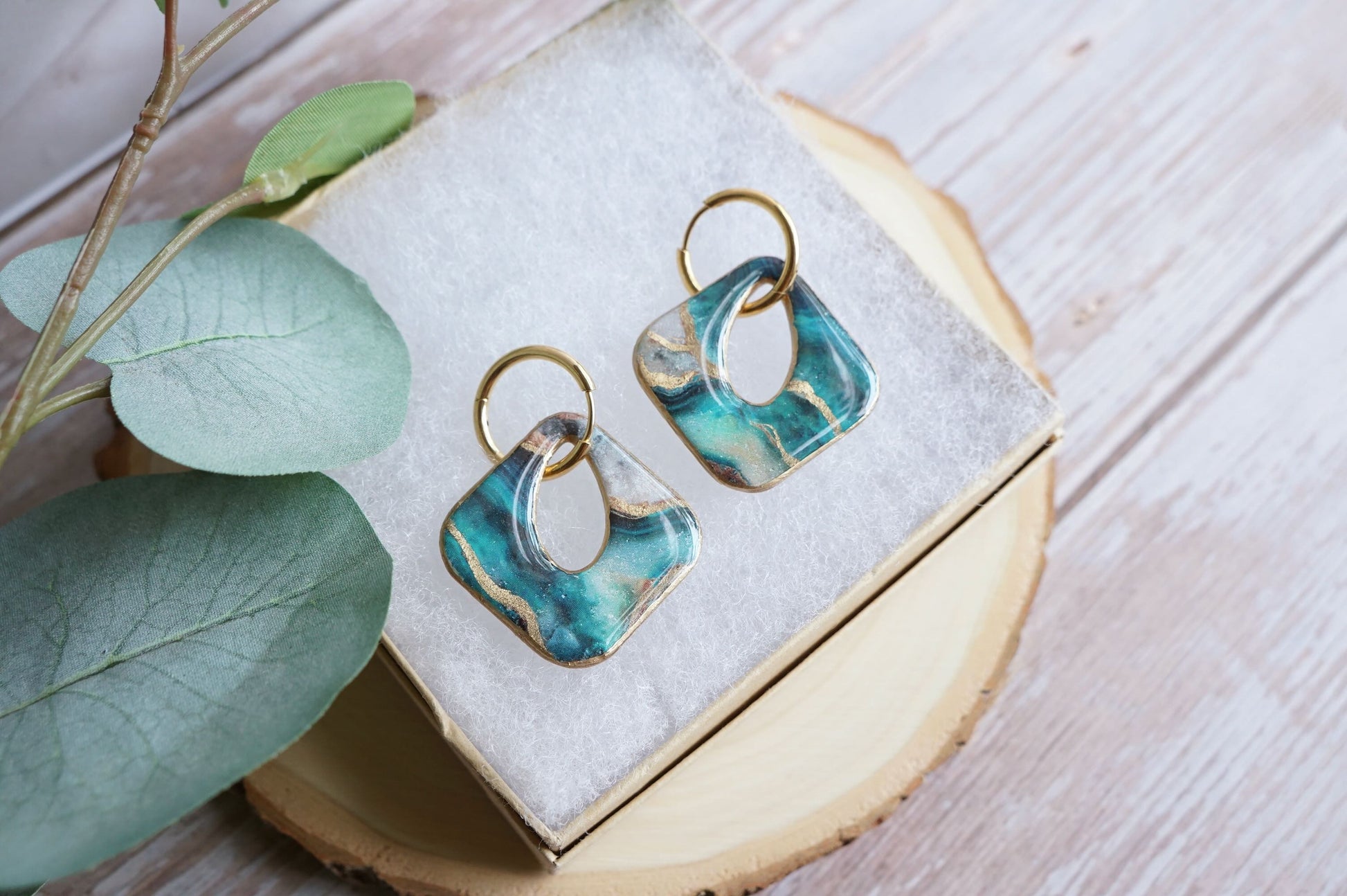 Artisan teal and gold earrings styled on soft fabric display
