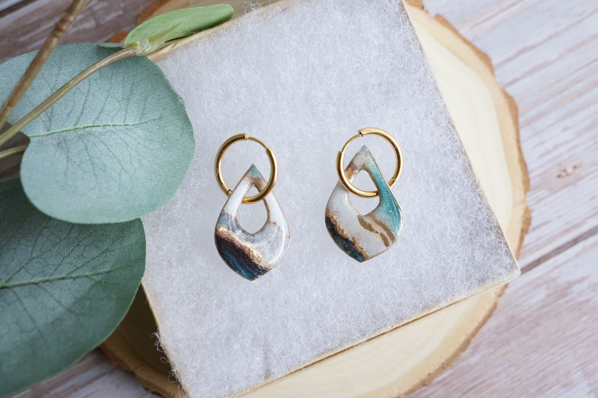 Artisan teal and gold earrings styled on soft fabric display