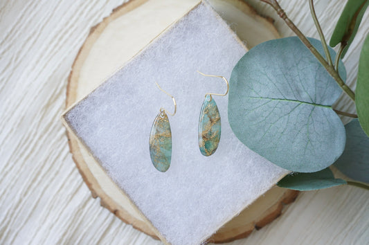 Handmade Gilded Tides Current earrings with elongated translucent turquoise polymer clay pendants, shimmering gold marbling and delicate gold-tone hooks.