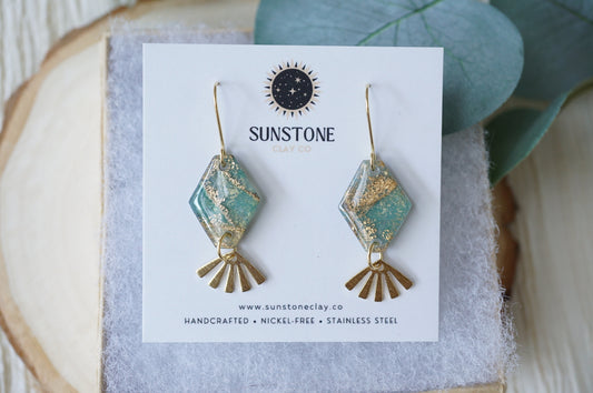 Handmade Gilded Tides Sunray Earrings with turquoise and shimmering gold marbled polymer clay diamond shapes and dangling gold fan charms, displayed on a Sunstone Clay Co jewelry card.