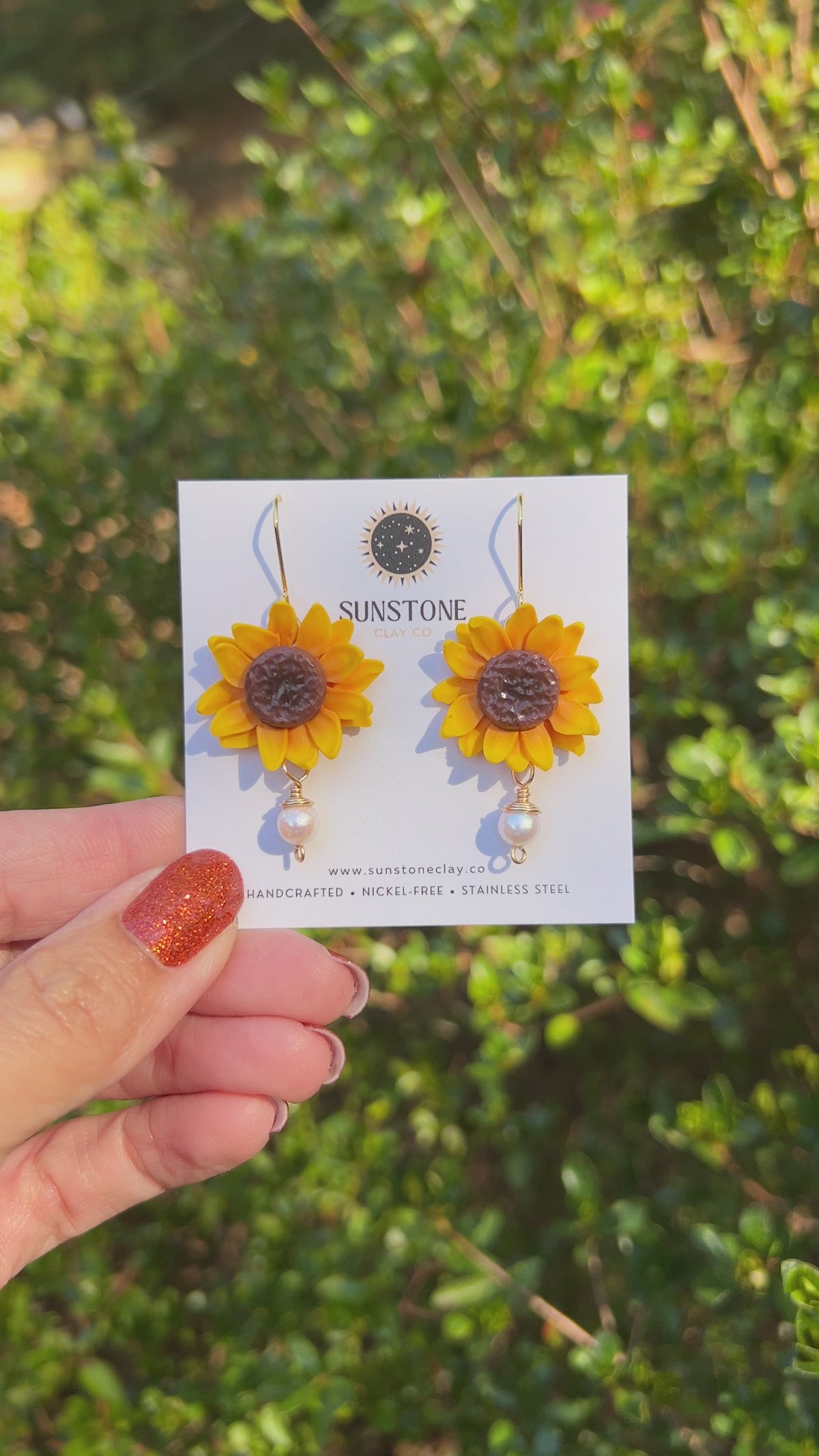 A video of handmade yellow polymer clay sunflower dangle earrings with textured brown centers, genuine pearl drops, and 18K gold-plated hooks by Sunstone Clay Co.