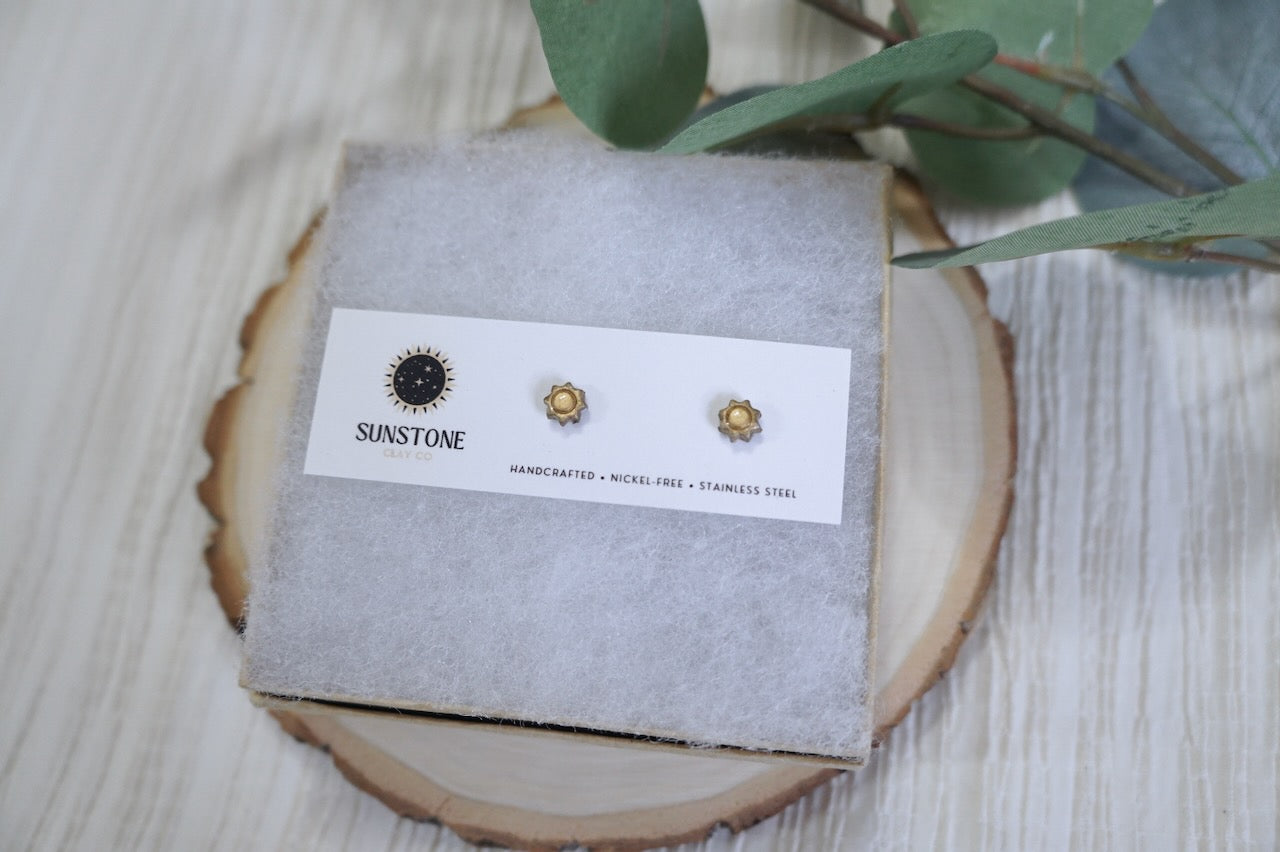Close-up of gold sunburst polymer clay stud earrings with stainless steel posts, handcrafted by Sunstone Clay Co.